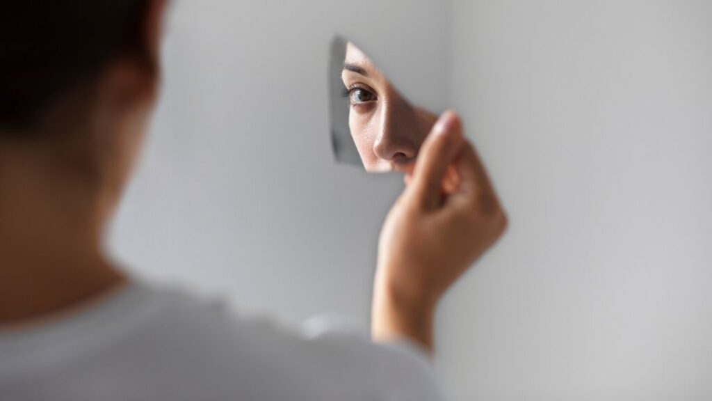 Triangulación narcisista: Persona mirando su reflejo en un trozo de espejo roto, simbolizando la introspección y el autoconocimiento