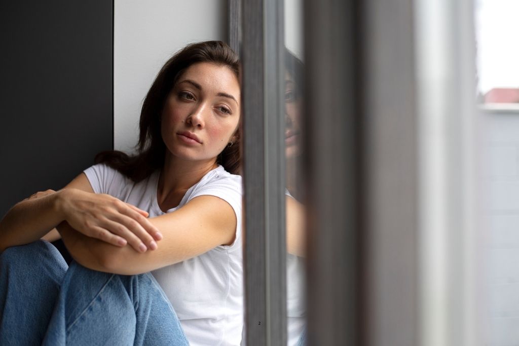 Bloqueo emocional: mujer sentada junto a una ventana con gesto pensativo y mirada triste